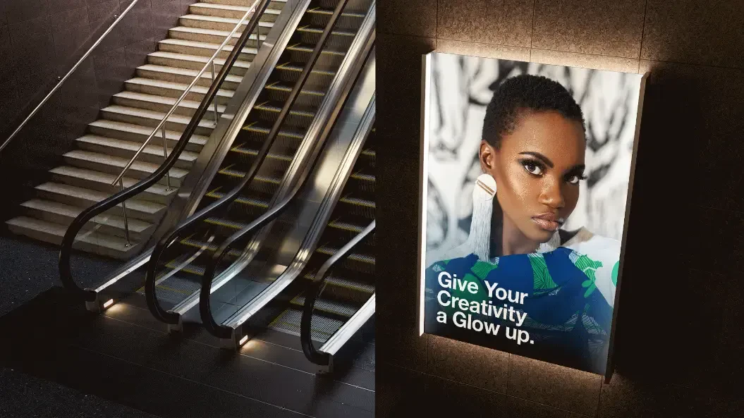 A backlit advertisiment on the wall by the escalators