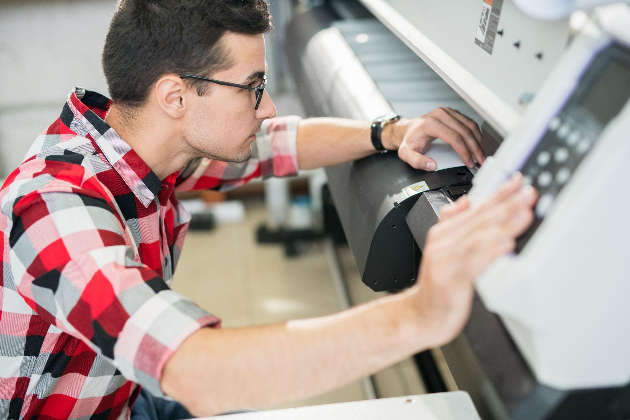 Serious young engineer examining wide format printer